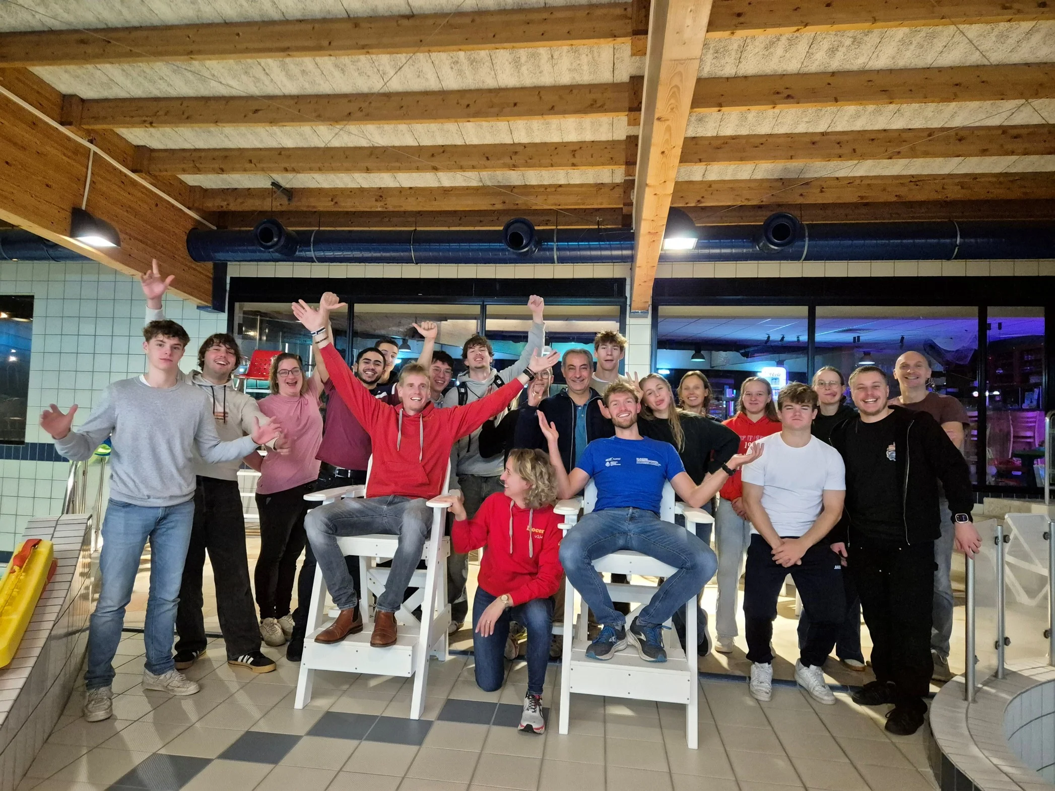 Een cursusgroep Hoger Redder juicht samen aan het zwembad, rond twee witte redderstoelen