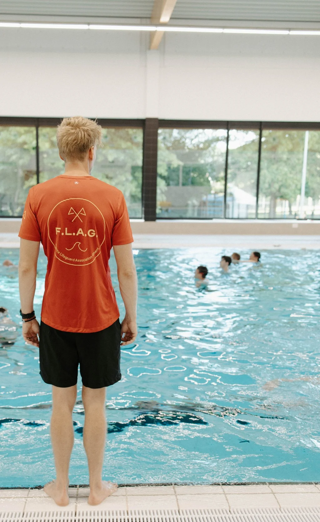 Een lesgever van FLAG kijkt vanaf de badrand naar de zwemmers in het water