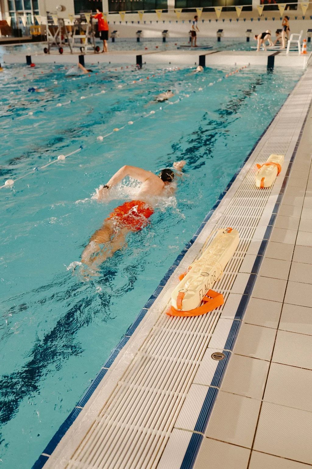 Een zwemmer in het wedstrijdbad, naast reddingsboeien en oefenpoppen op de badrand