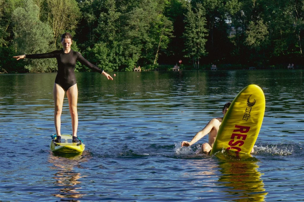 Een redder staat rechtop op een rescue board, naast iemand die met een board in het water valt