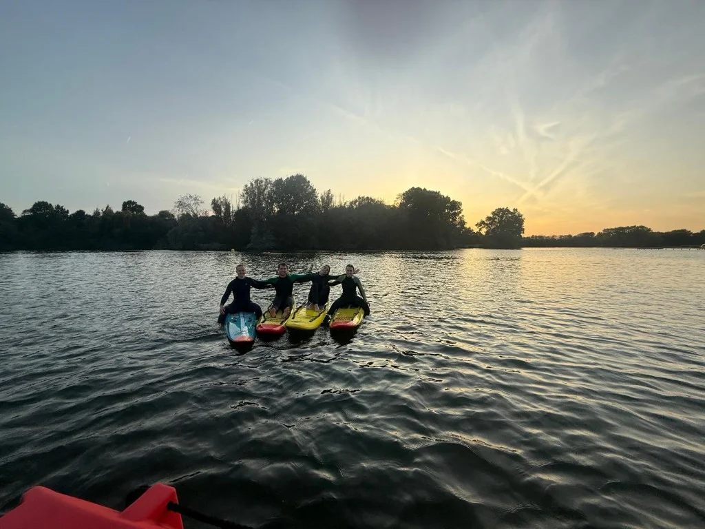 Vier redders zitten arm in arm op hun rescue boards op het meer bij zonsondergang